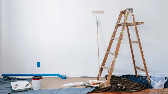 롤러, 사다리, 페인트통이 놓인 방 안의 페인트 작업 재료들